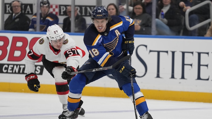 Deux joueurs de hockey d'équipes adverses tentent de maîtriser une rondelle.