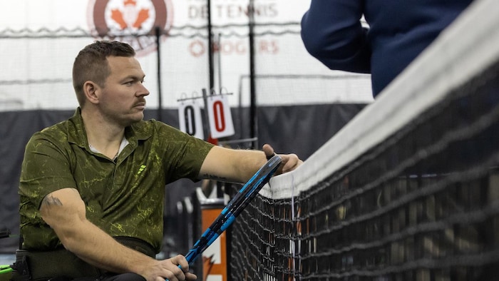 Un athlète en fauteuil roulant près d'un filet de tennis.