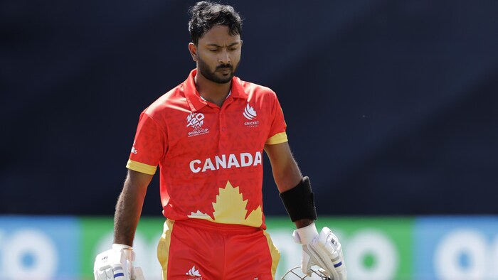 Un joueur en rouge marche sur un terrain de cricket.