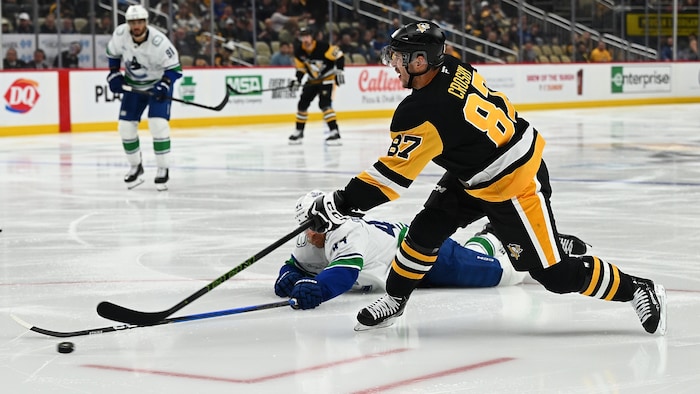 Un joueur de hockey tente un tir alors que son adversaire tente de le bloquer.