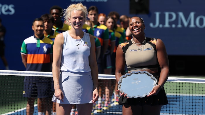 Deux joueuses de tennis sourient et l'une d'elles tient un trophée. 