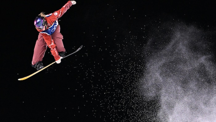 Une planchiste vient de sauter dans les airs avec une grande traînée de neige derrière elle.