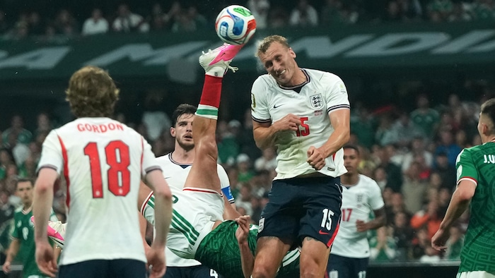 Un joueur de soccer tente un retourné acrobatique pendant qu'un défenseur essaie de dégager le ballon de la tête.
