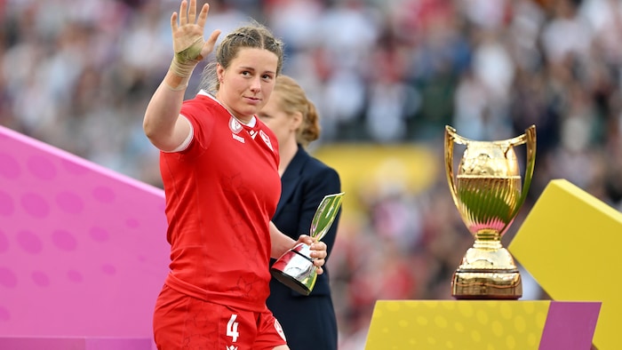 Avec un trophée en or dans la main gauche, elle salue la foule de l'autre.