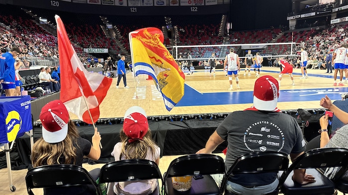 Jeunes filles avec des casquettes du Canada brandissent un drapeau canadien et un autre du Nouveau-Brunswick.