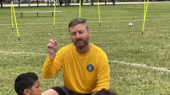 Frédéric Boulanger, responsable de Beyond Sports Soccer Academy, est accroupi sur un terrain pendant les entraînements avec les enfants.