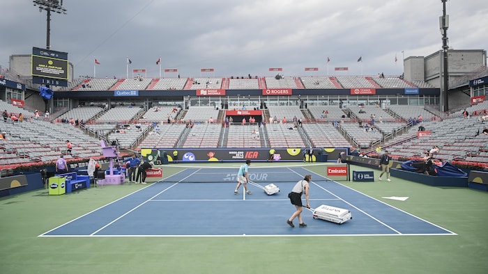Deux personnes assèchent un terrain de tennis avec des machines. 