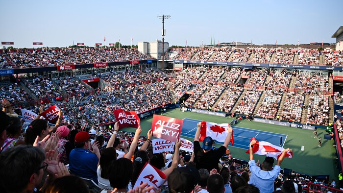 Des partisans dans un stade de tennis agitent des drapeaux canadiens. 
