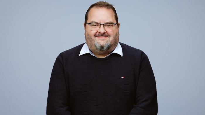 L'homme regarde la caméra en souriant.