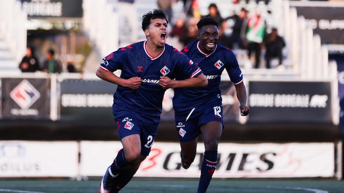 Un joueur de soccer crie de joie en tenant son maillot avec ses mains.
