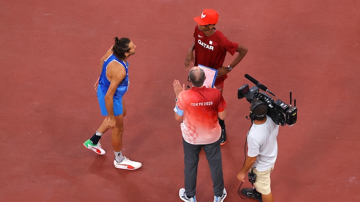 Deux athlètes discutent avec un arbitre et une caméra de télévision les filme.