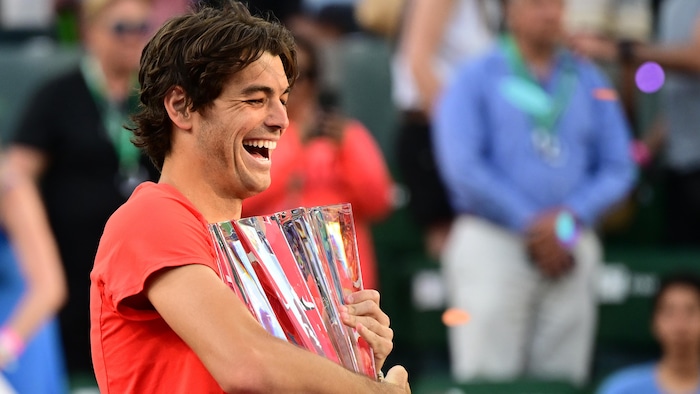 Showing a broad smile, he holds the trophy.