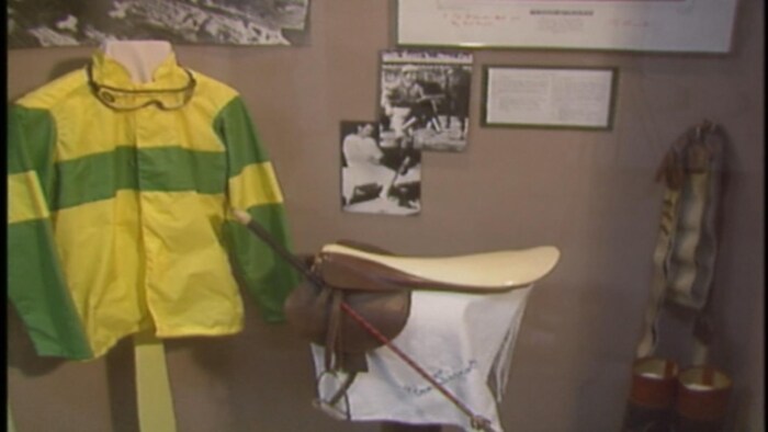 Manteau, selle, bottes et cravaches mis en exposition dans une vitrine.