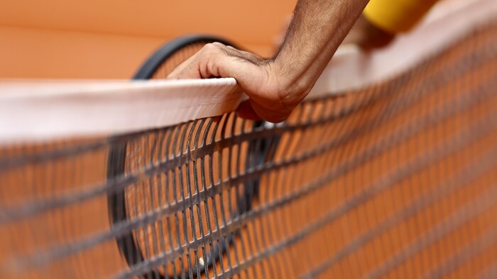 Les mains d'un joueur de tennis sont appuyées contre le filet sur un terrain de terre battue.