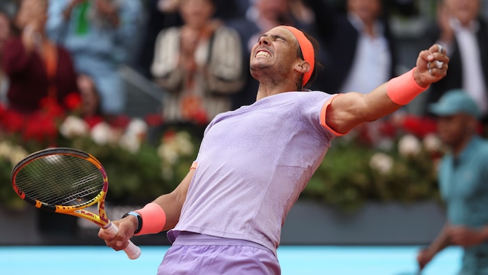Les bras en croix, un joueur de tennis exprime sa joie après la victoire en serrant le poing gauche et en tenant sa raquette de la main droite.