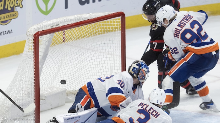 Un joueur de hockey déjoue un gardien devant deux adversaires.