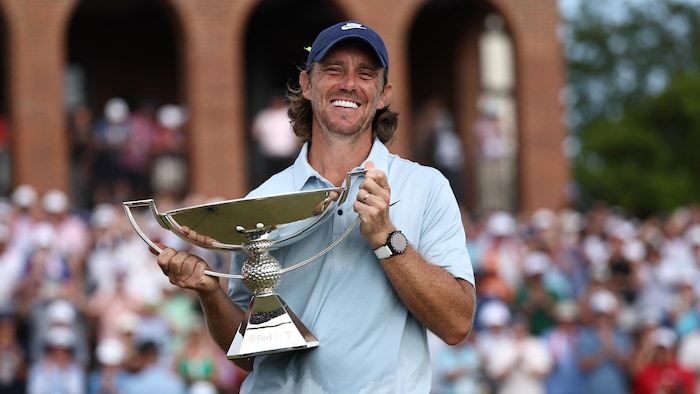 Un golfeur sourit à pleines dents en tenant un trophée dans ses mains.
