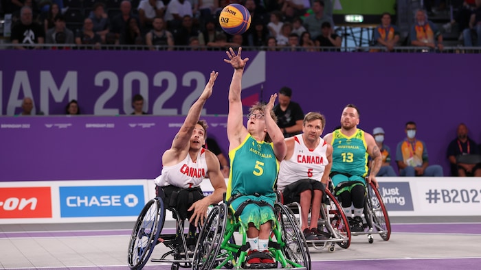 Un basketteur en fauteuil roulant décoche un lancer pendant qu'il est pourchassé par un adversaire.