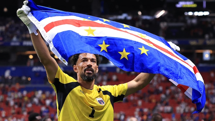Un gardien au soccer montre fièrement le drapeau de son pays.