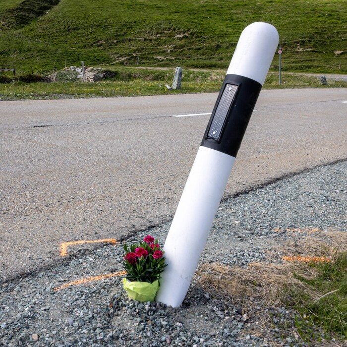 Une gerbe de fleurs se trouve au sol, en bordure d'une route en pente.