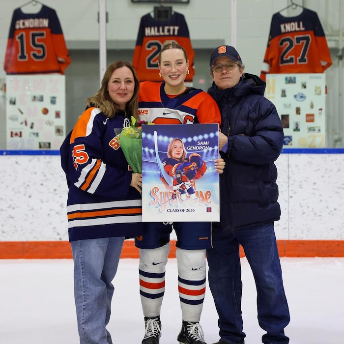 Une joueuse de hockey pose sur la patinoire avec ses parents.