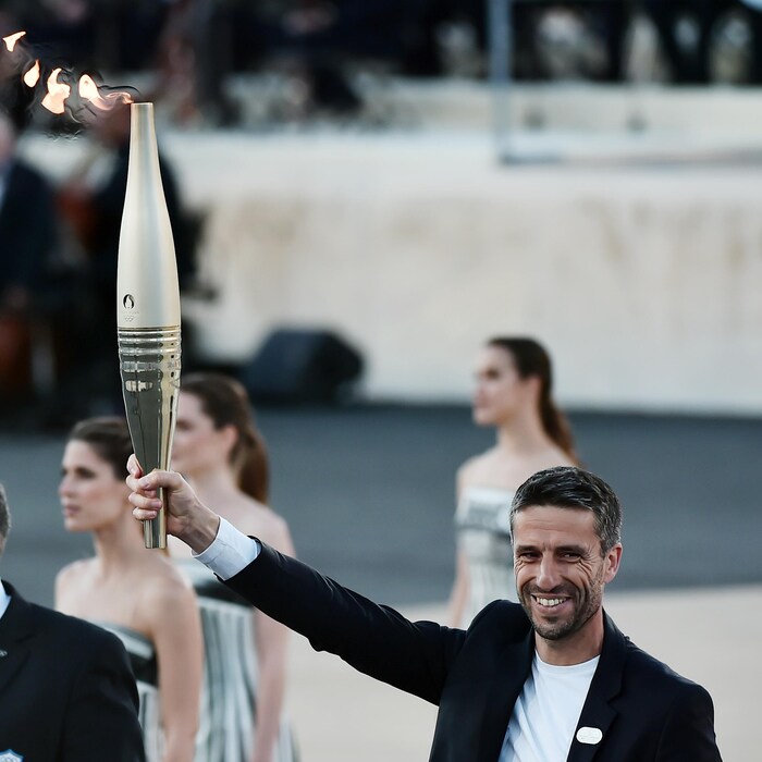 Un homme souriant tient au bout de son bras droit un flambeau allumé.