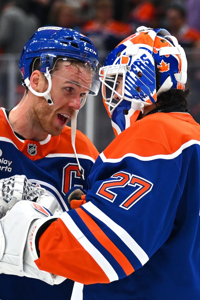 Un joueur de hockey sourit en regardant son coéquipier gardien de but. 