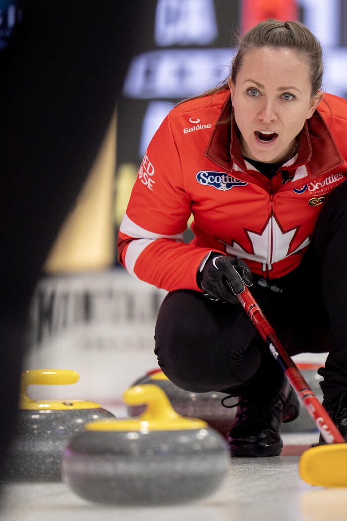 Une joueuse de curling avec son balai, devant des pierres.