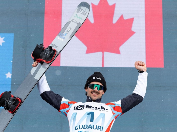 A skater raises his arms to the sky, and behind him we see the Canadian flag displayed on the screen.