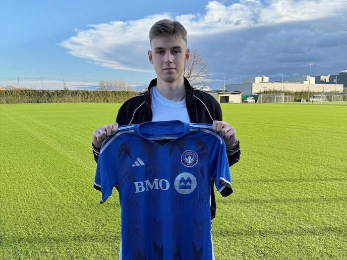Un athlète tient un chandail bleu près d'un terrain de soccer.