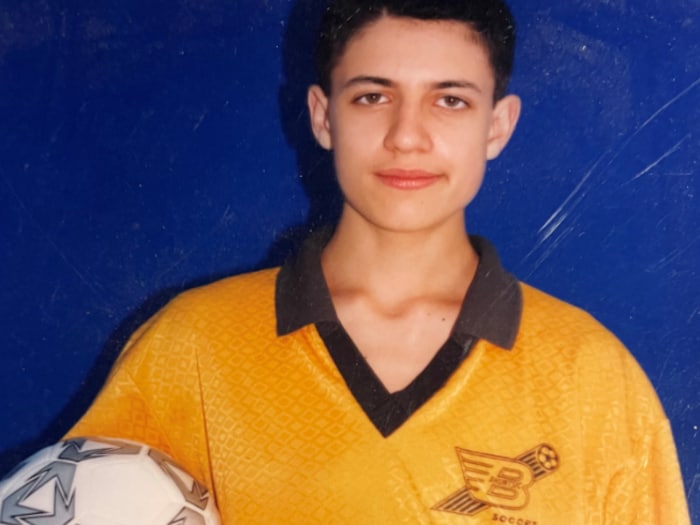 Le garçon, vêtu d'un uniforme de soccer, tient un ballon dans son bras droit.
