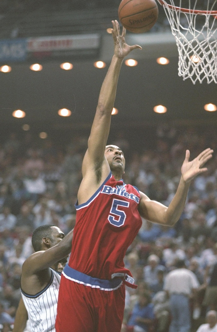 Un joueur de basketball, vêtu d'un uniforme rouge, dépose le ballon dans le panier lors d'un match de la NBA. 