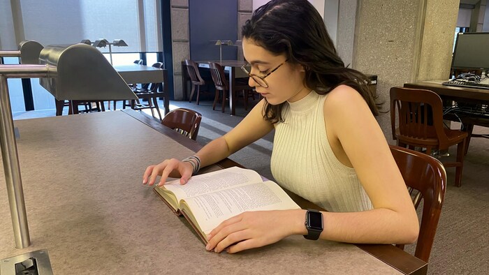 Une femme (Maya Larrondo, petite-fille d'exilés chiliens au Canada et étudiante en anthropologie médico-légale à l'université de Toronto) lit un livre dans une bibliothèque. 