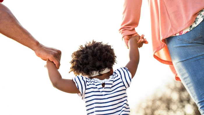 Une petite fille (de dos) tient la main de deux adultes.