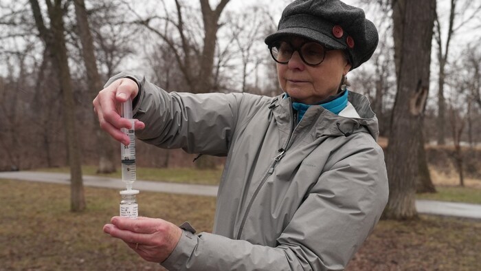 Une femme manipule une seringue dans un parc. 