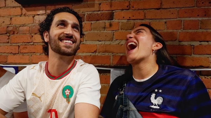 Un homme portant les couleurs du Maroc et une femme portant celles de la France rient.