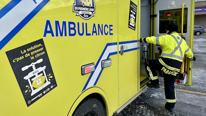 Une technicienne ambulancière paramédicale monte à bord d'une ambulance, côté passager.