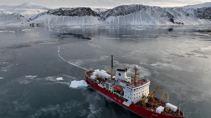Un navire blanc et rouge flottant sur des eaux calmes et parsemées de glace