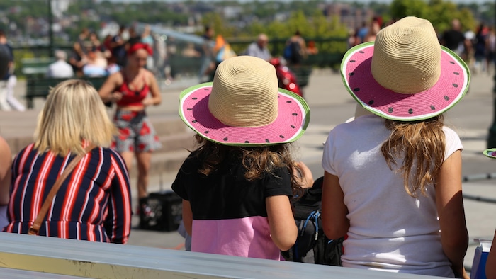 Trois personnes sont assises et profitent de la performance d'amuseurs publics par une journée ensoleillée.