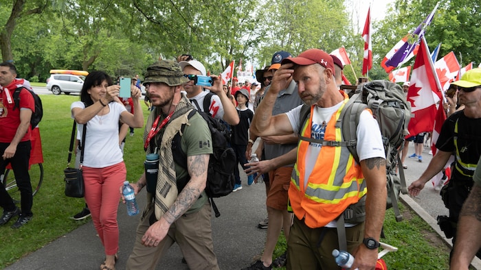 Veteran James Topp, in the orange vest, is flanked by supporters as he arrives at Hog's Back Park in Ottawa on June 30, 2022. Topp marched across the country to protest remaining COVID-19 vaccine mandates.