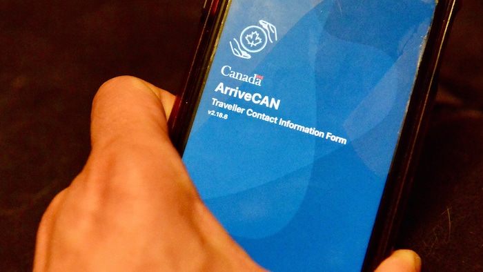 Une main tient un téléphone sur lequel apparaît l'application ArriveCAN.