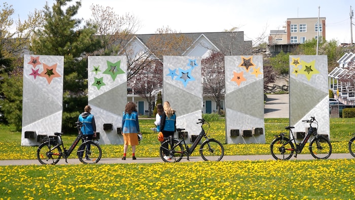 Des personnes descendues de leur vélo regardent une sculpture monumentale dans un parc.