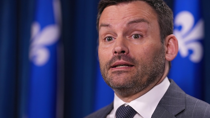 Le chef du Parti québécois, Paul St-Pierre Plamondon, se tient à devant des drapeaux du Québec.