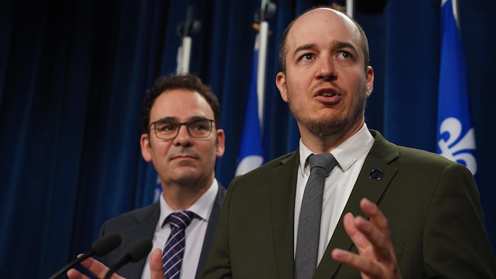deux hommes en costume-cravate parlent durant une conférence de presse