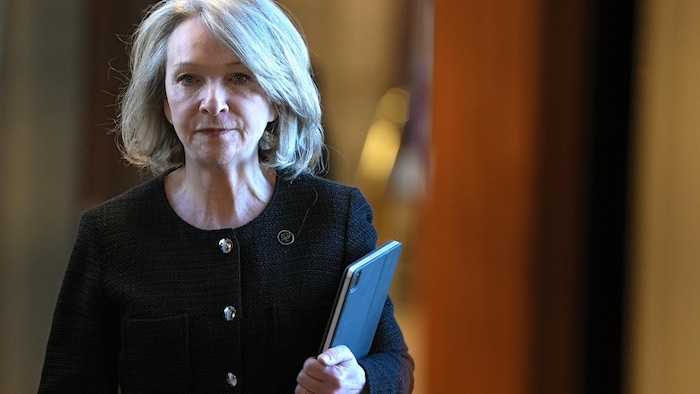 Sonia Bélanger, dossiers à la main, marche dans un corridor. 