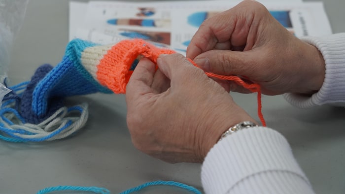 Une fermière tricote une poupée avec des aiguilles et de la laine.