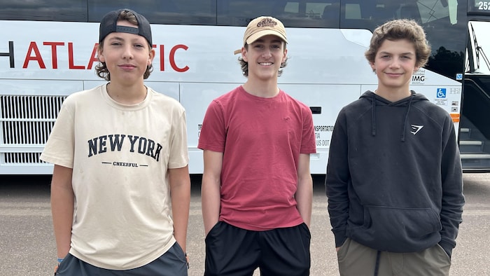 Trois élèves sourient à la caméra, devant un autocar.