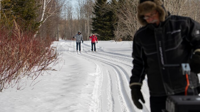 Un bénévole trace les pistes au premier plan, avec, derrière, deux skieurs qui avancent dans les pistes.