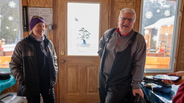 Une femme et un homme se tiennent devant une porte vitrée, à l'intérieur d'un chalet lumineux.