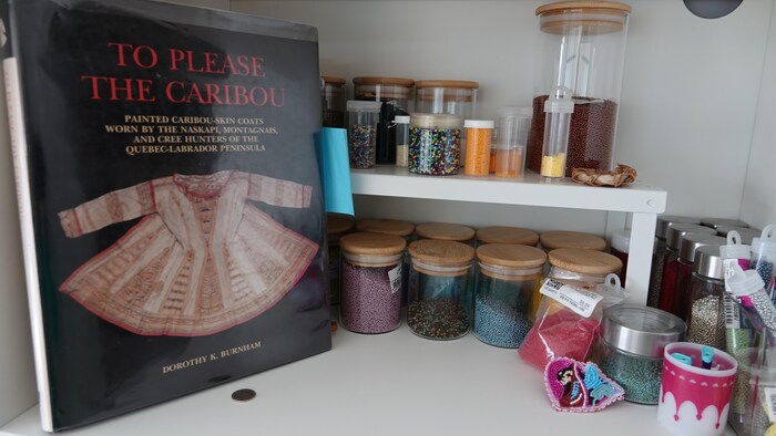 Le livre « To please the caribou » et des perles rangées dans des bocaux se trouvent sur un comptoir.
